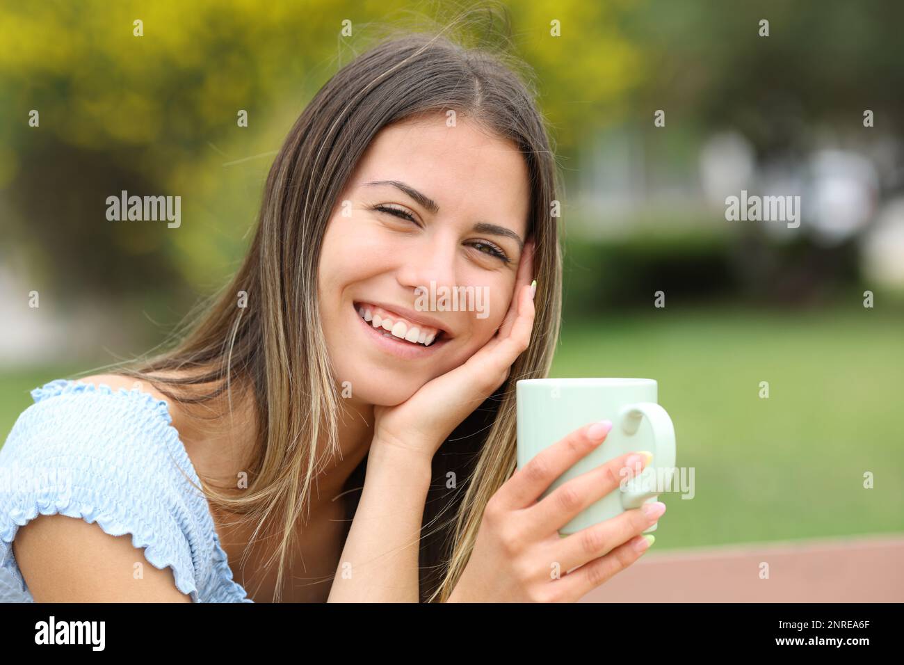 Candid happy teen looks at you holding coffee mug in a park Stock Photo