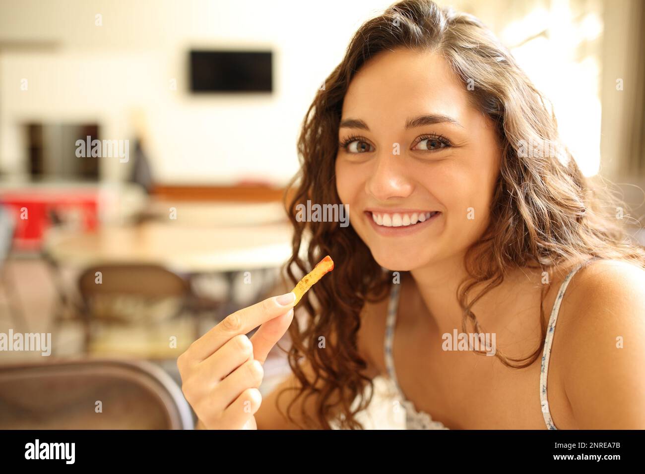 Happy woman in a coffee shop eating potatoe and looking at camera Stock Photo