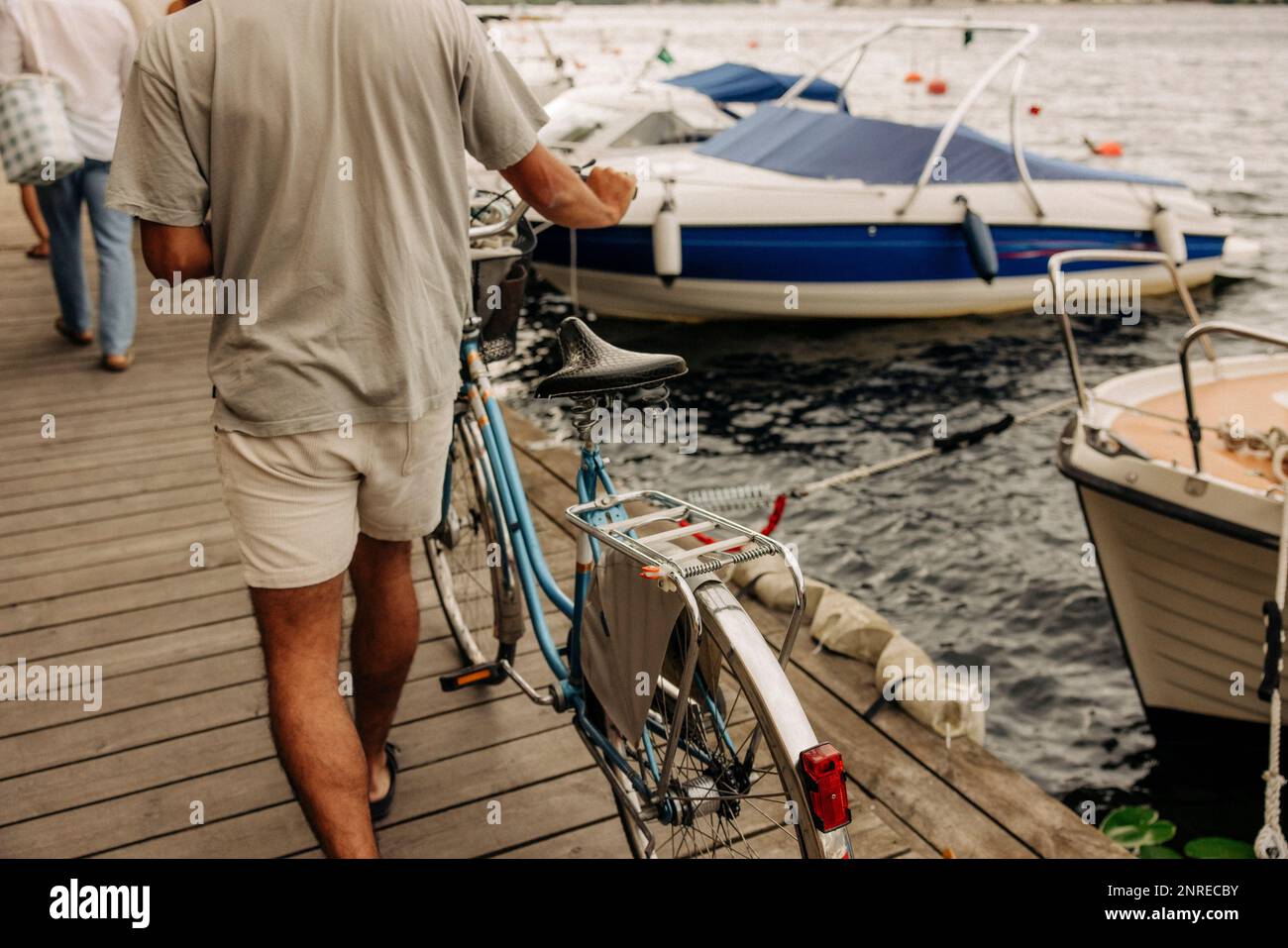 Rear view of man wheeling bicycle on pier at harbor Stock Photo