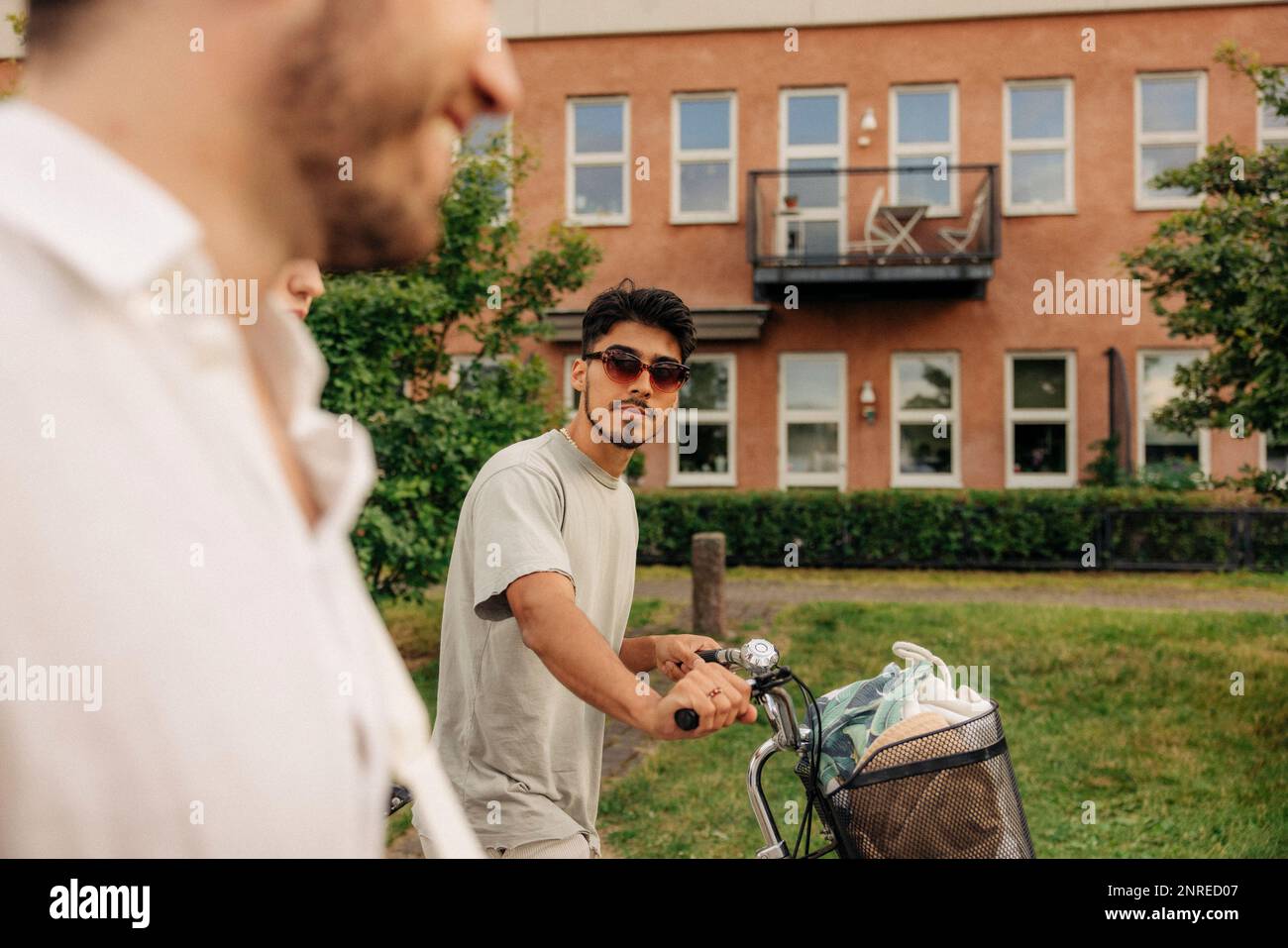 Young man wearing sunglasses while wheeling bicycle walking with friend Stock Photo