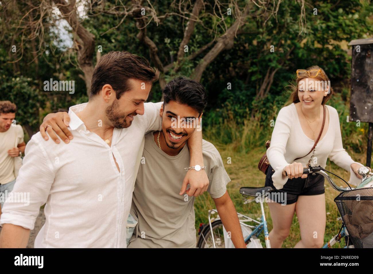 Happy woman with bicycle looking at male friends walking together Stock Photo