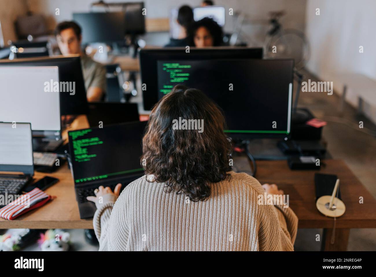 Rear view of young female programmer coding on computer at desk in ...