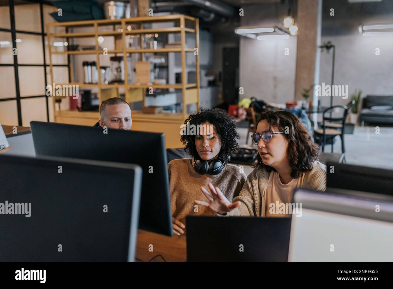 Young female hacker explaining strategy to colleagues over computer while working in office Stock Photo