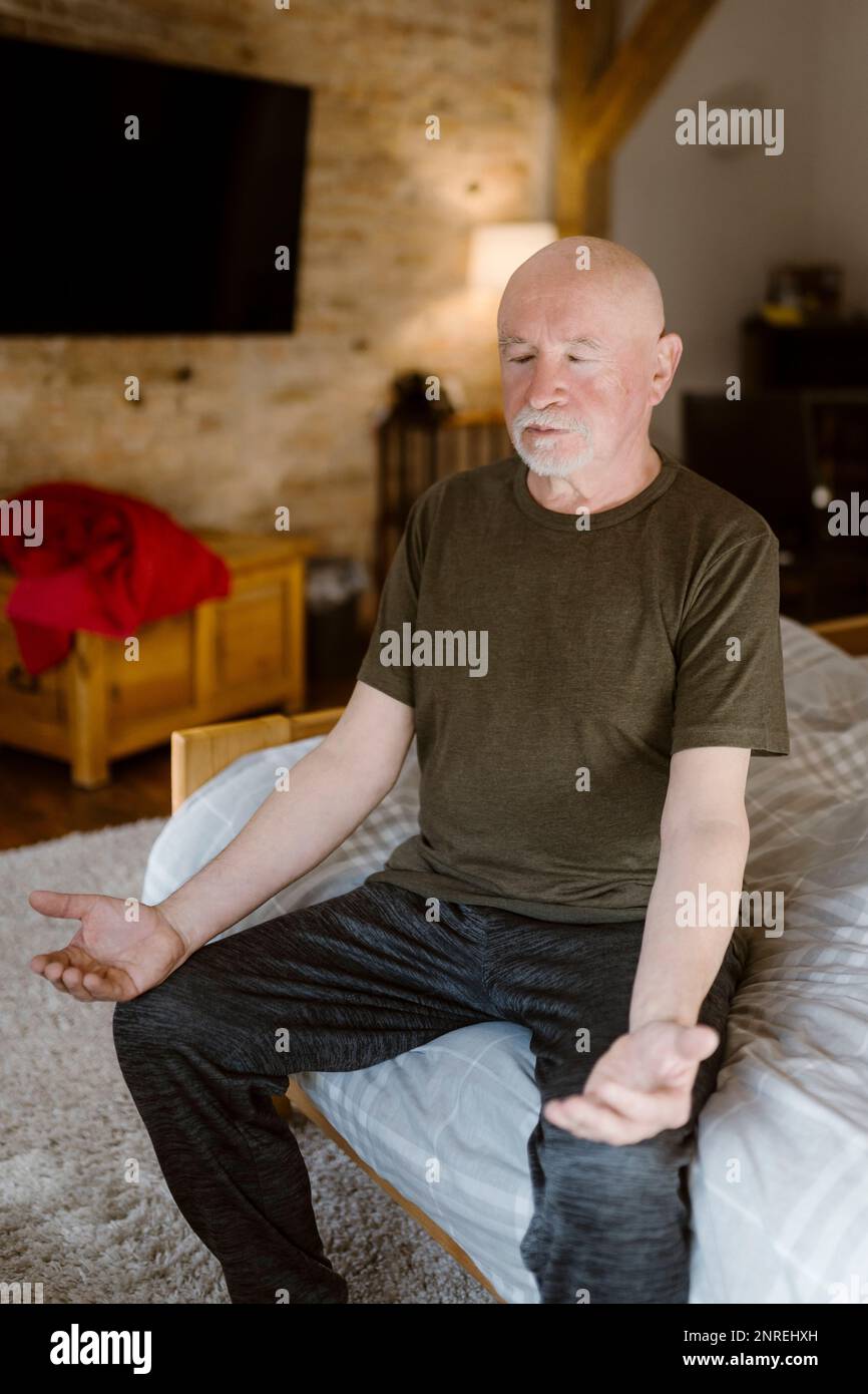 Senior man practicing yoga while sitting on bed at home Stock Photo