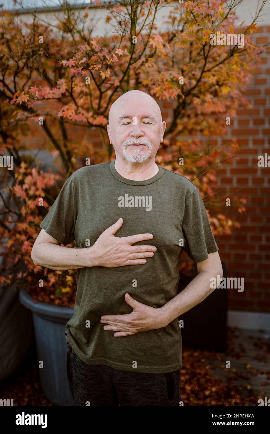 Senior man doing breathing exercise while standing against plant Stock Photo