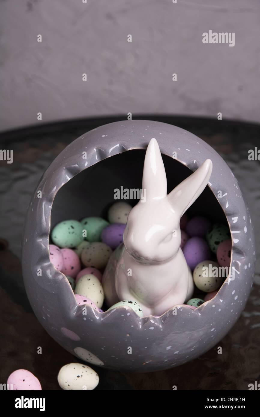 photo in a large gray decorative egg is a lot of multi-colored decorative small eggs and sits a white rabbit Stock Photo