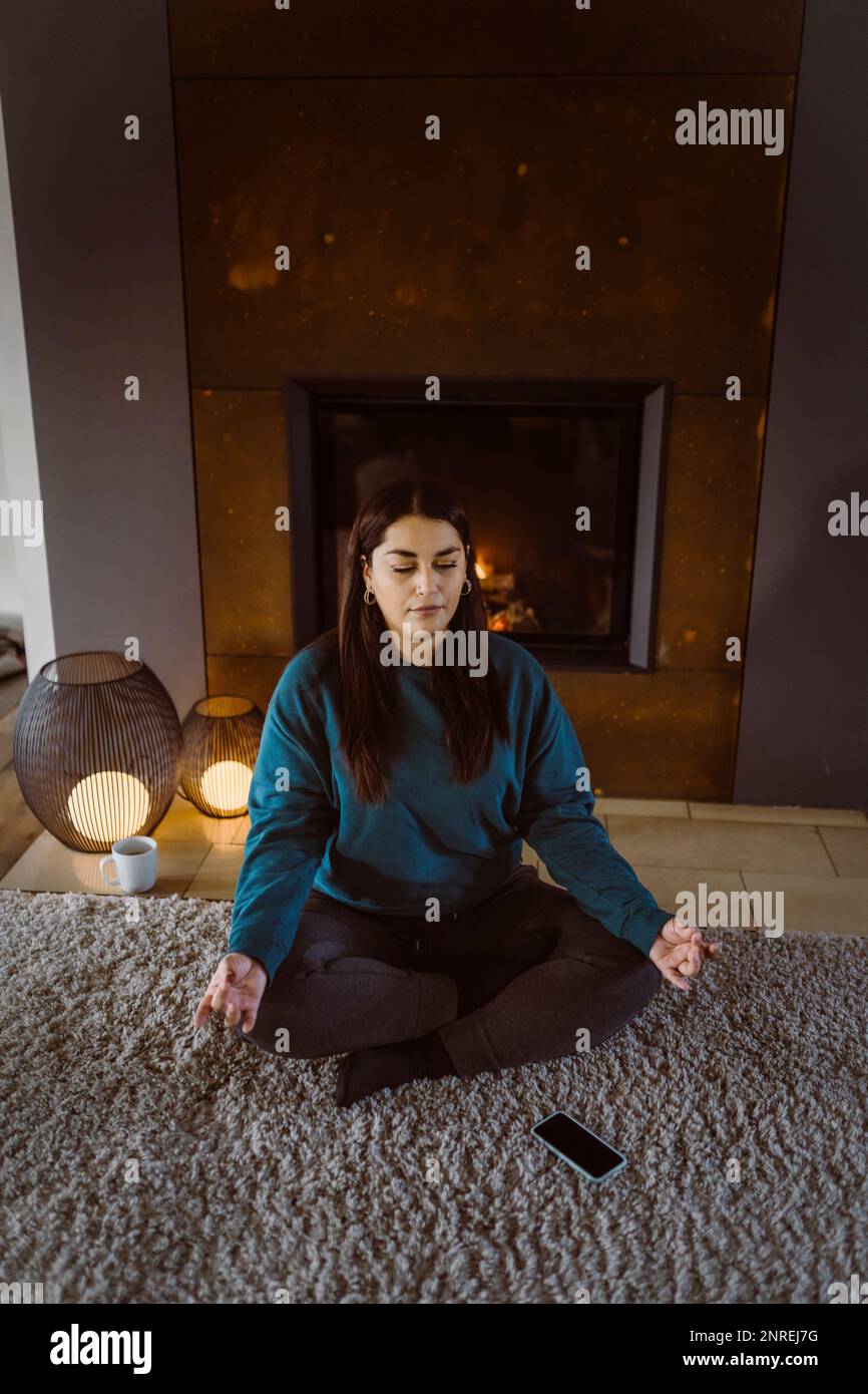Woman practicing yoga while sitting cross-legged on carpet at home Stock Photo