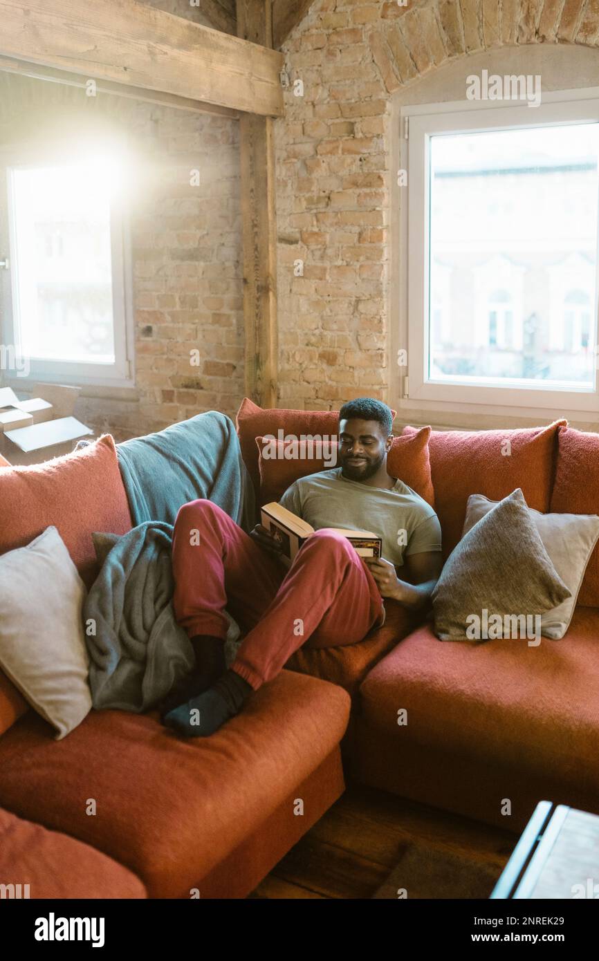 Young man reading book while relaxing on sofa at home Stock Photo