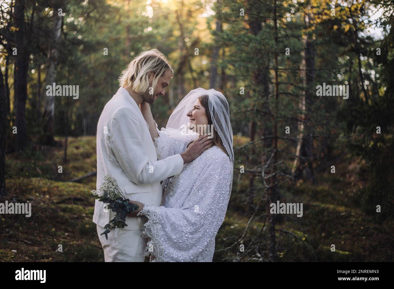 Smiling newly married couple looking at each other in forest during wedding Stock Photo