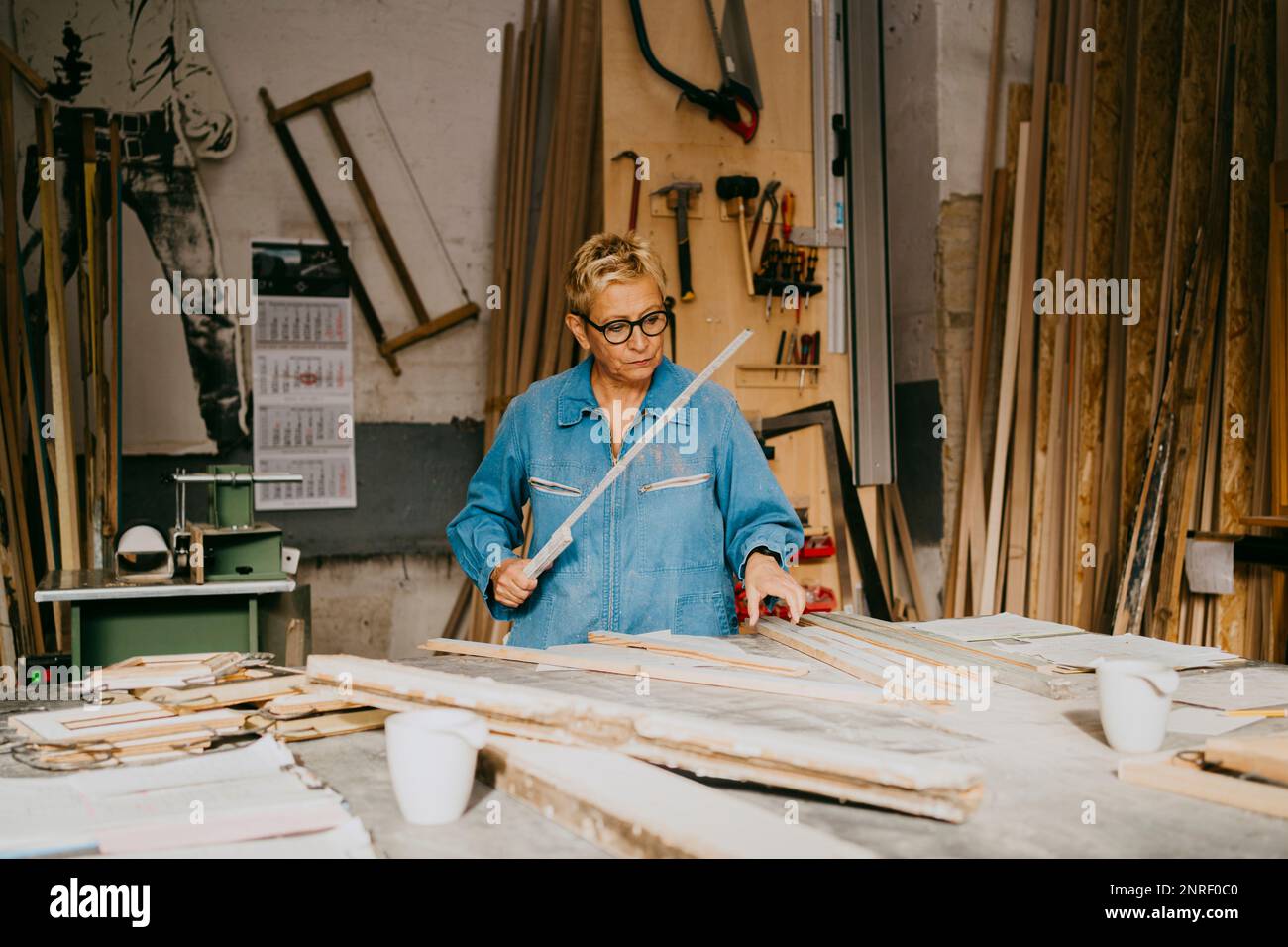 Senior craftswoman measuring timber on workbench at repair shop Stock Photo