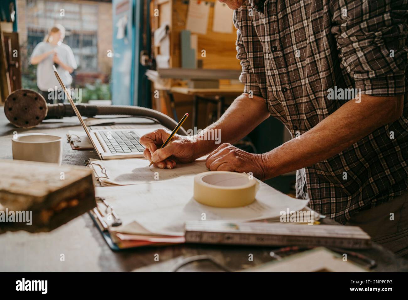 Midsection of craftsman preparing document by laptop at carpentry workshop Stock Photo