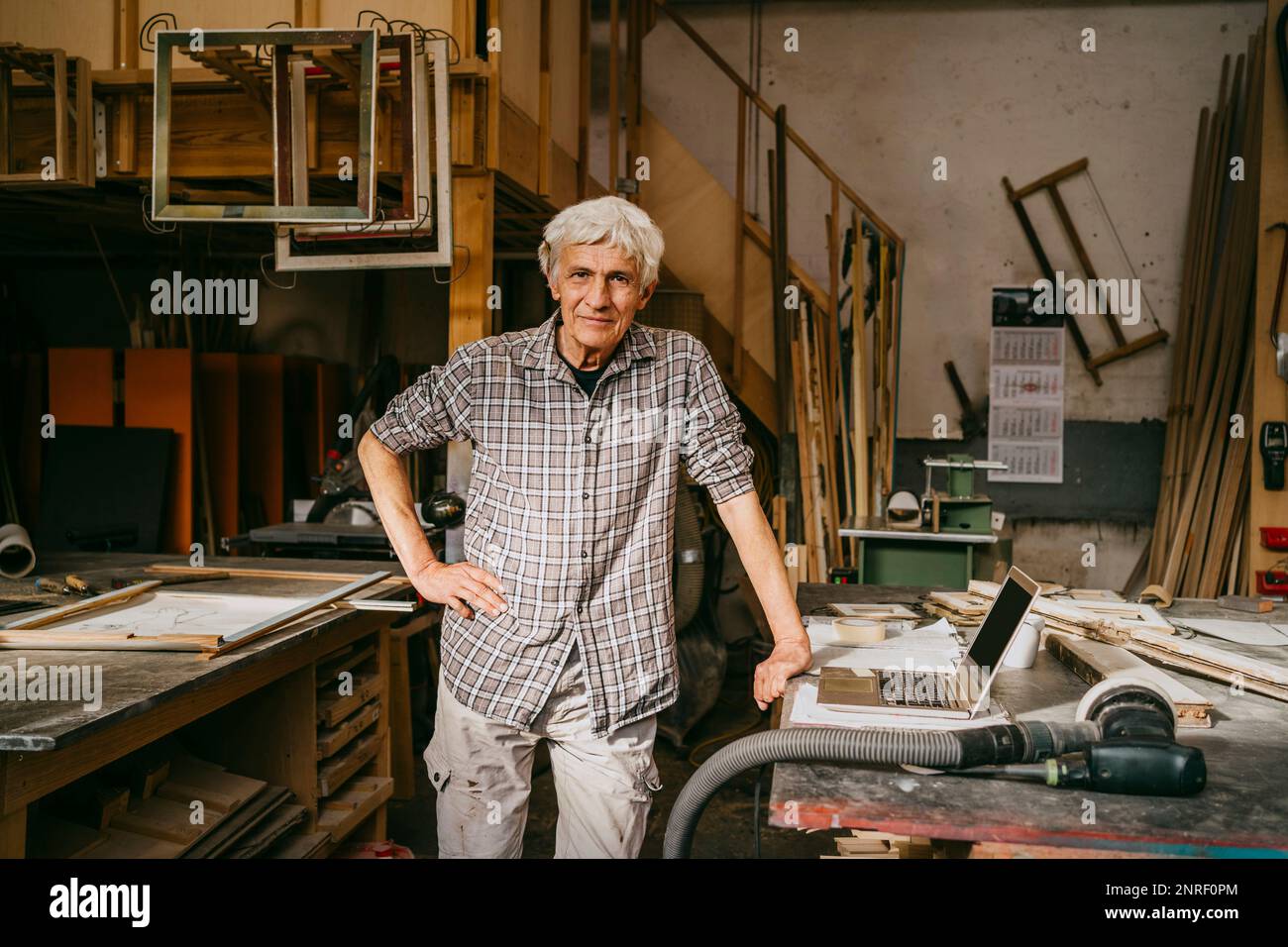 Portrait of male senior carpenter standing with hand on hip at workshop Stock Photo
