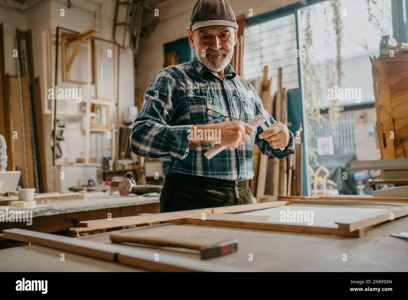 Focused senior male carpenter holding measuring tape at workshop Stock Photo