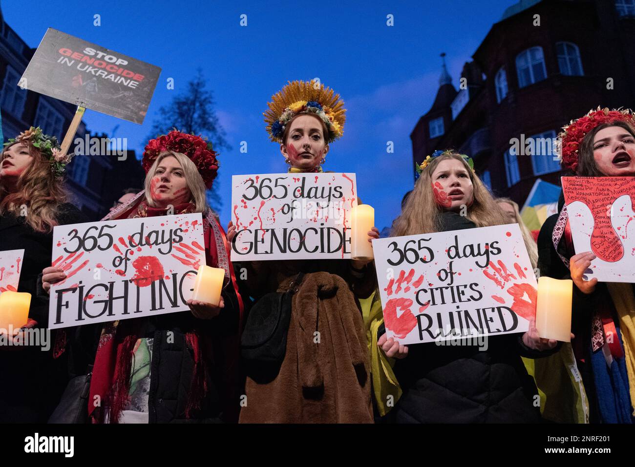 London, UK. 24 February, 2023. Ukrainian women wearing head dresses, faces covered in fake blood, pose with placards outside the Russian embassy durin Stock Photo
