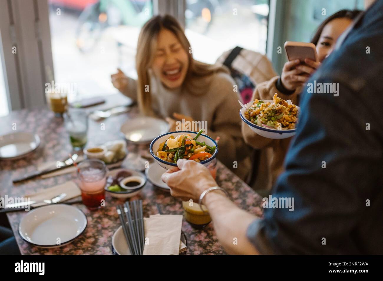 Waiter serving Chinese food to customers sitting at restaurant Stock