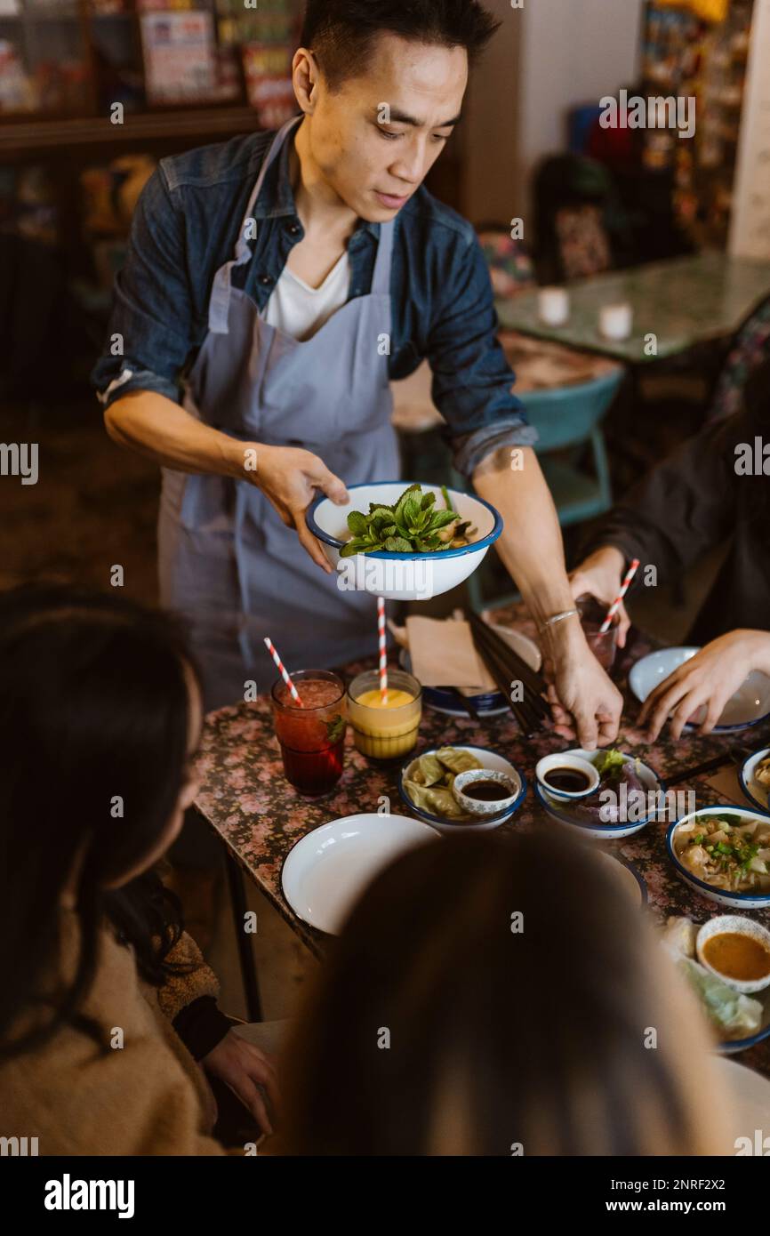 Waiter serving serving food and dumplings to customers at restaurant Stock Photo
