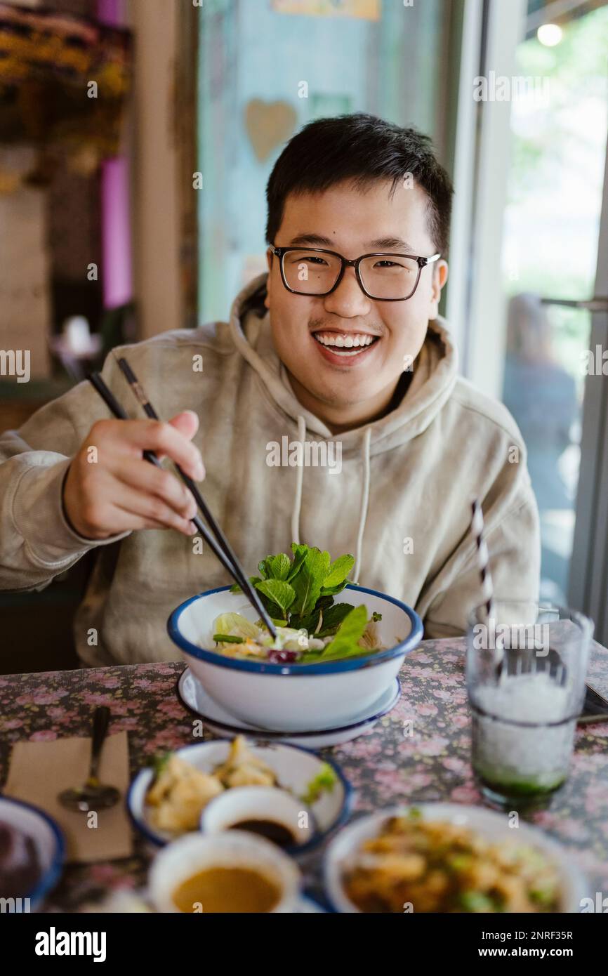 Portrait of smiling young man with food holding chopsticks at