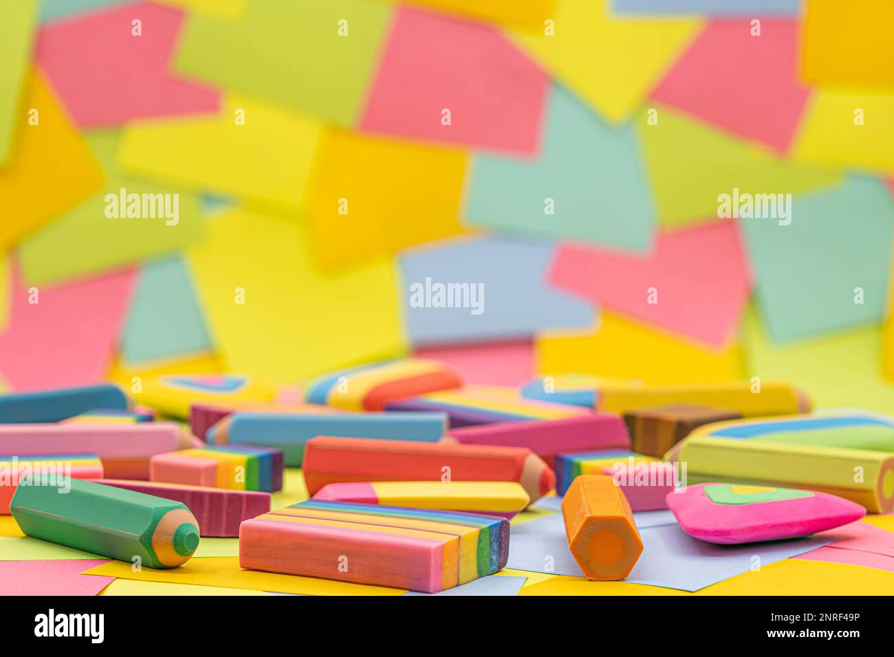 various shapes and colors of erasers arranged on a table with multicolored paper sticky notes on background Stock Photo