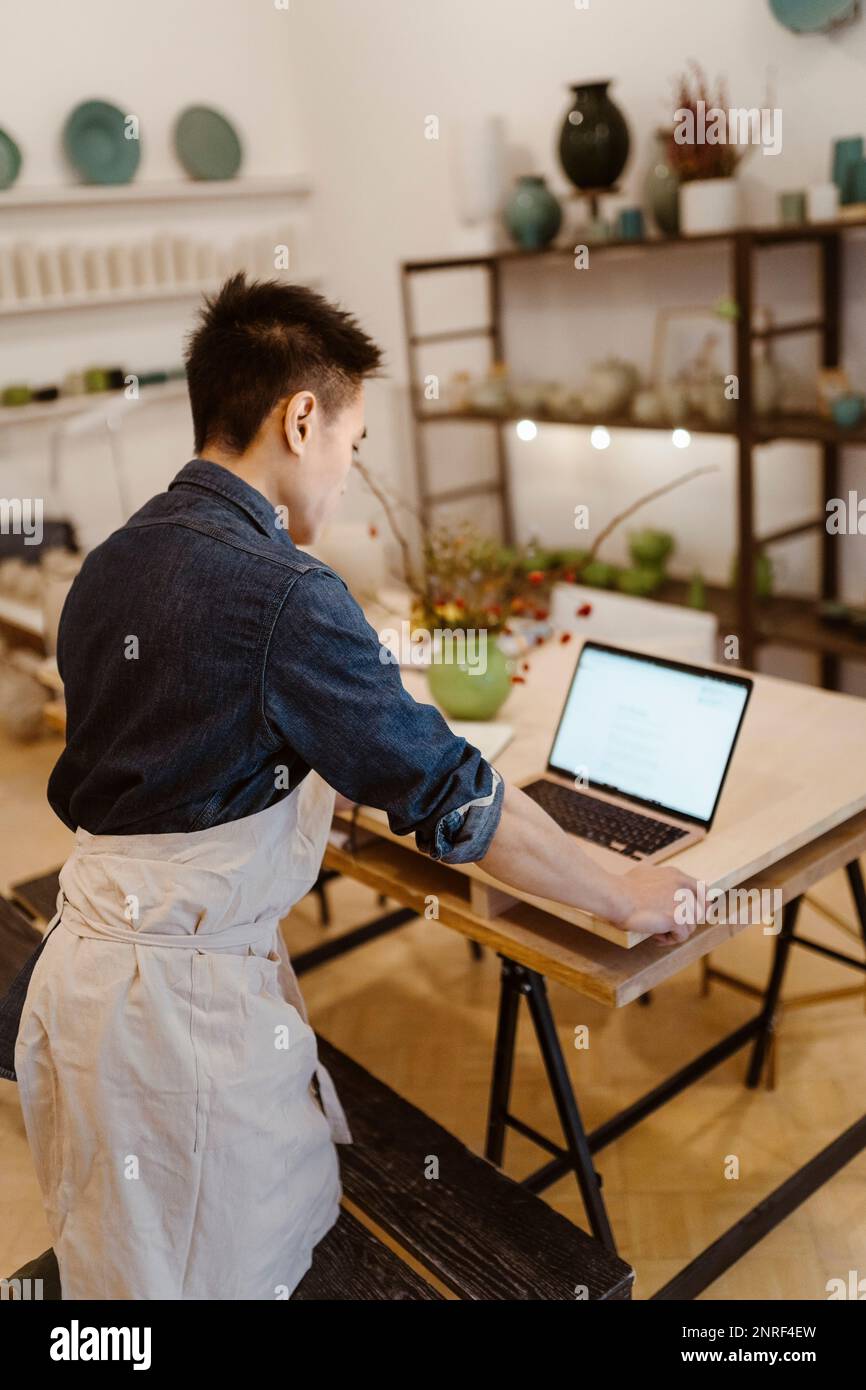 Male potter working on laptop while standing at workshop Stock Photo