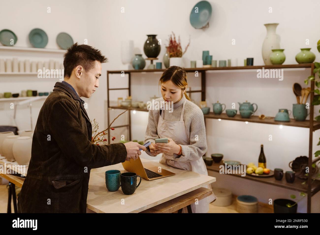 Side view of male customer paying through smart phone at pottery shop Stock Photo