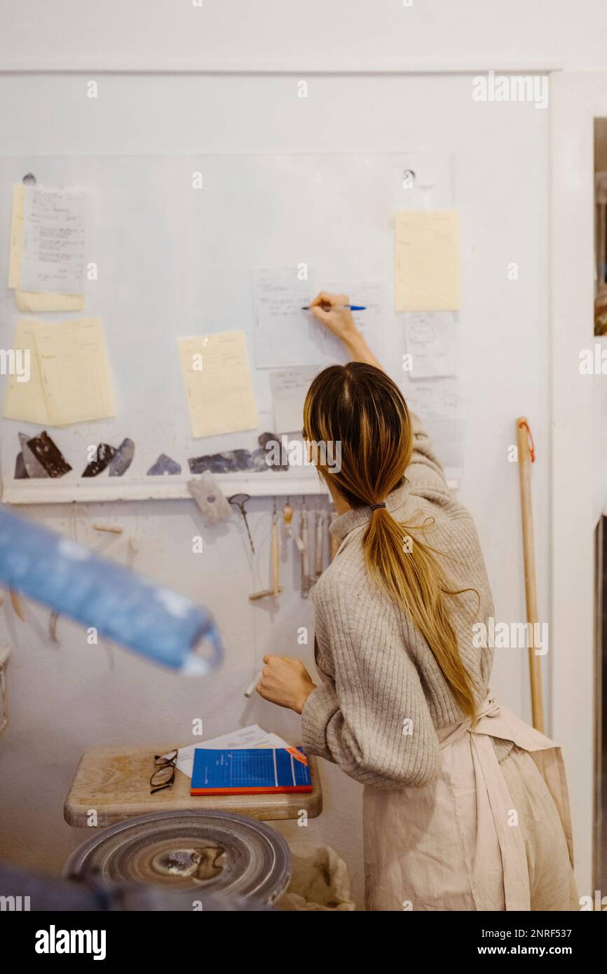 Female potter writing on paper while standing at workshop Stock Photo