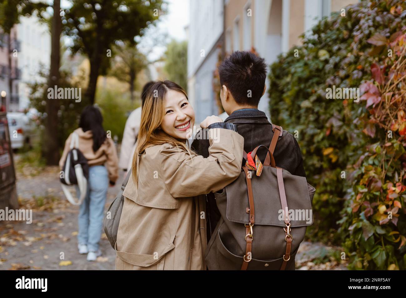 Portrait of happy woman looking over shoulder while walking with male friend on sidewalk Stock Photo
