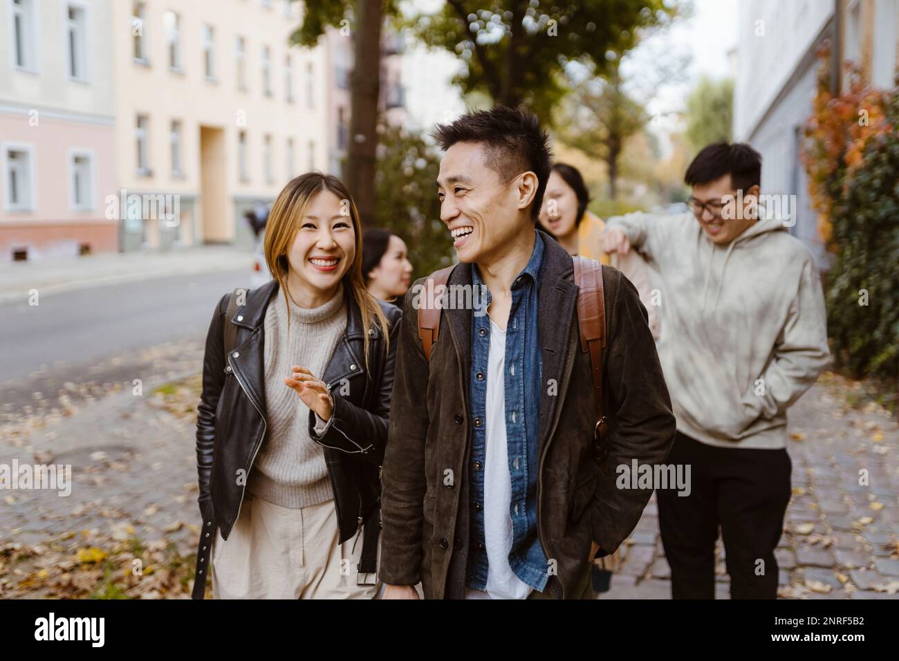 Male and female friends laughing while walking on sidewalk Stock Photo