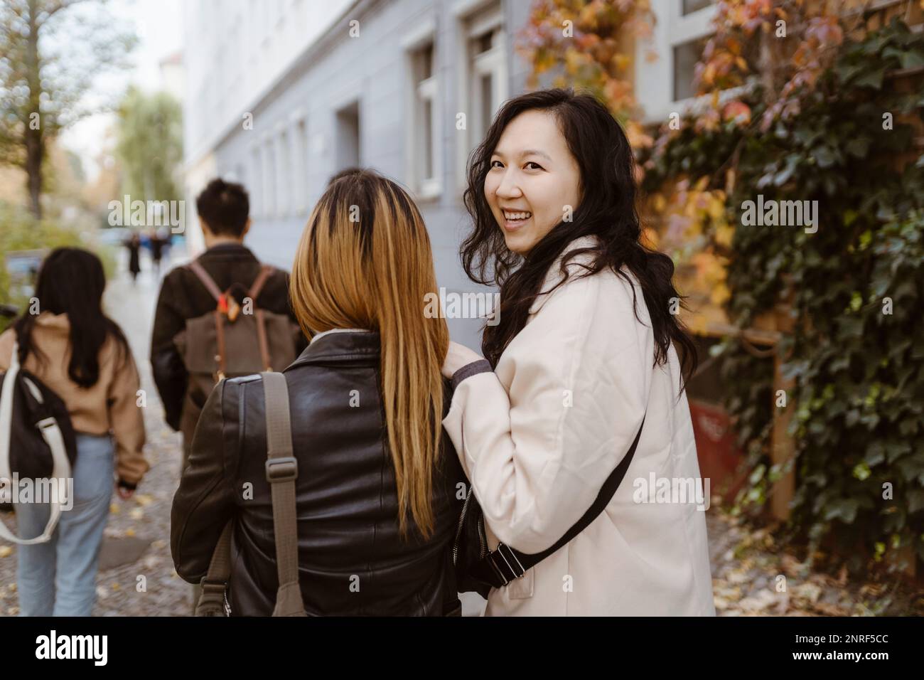 Happy woman looking away while walking with female friend on sidewalk Stock Photo