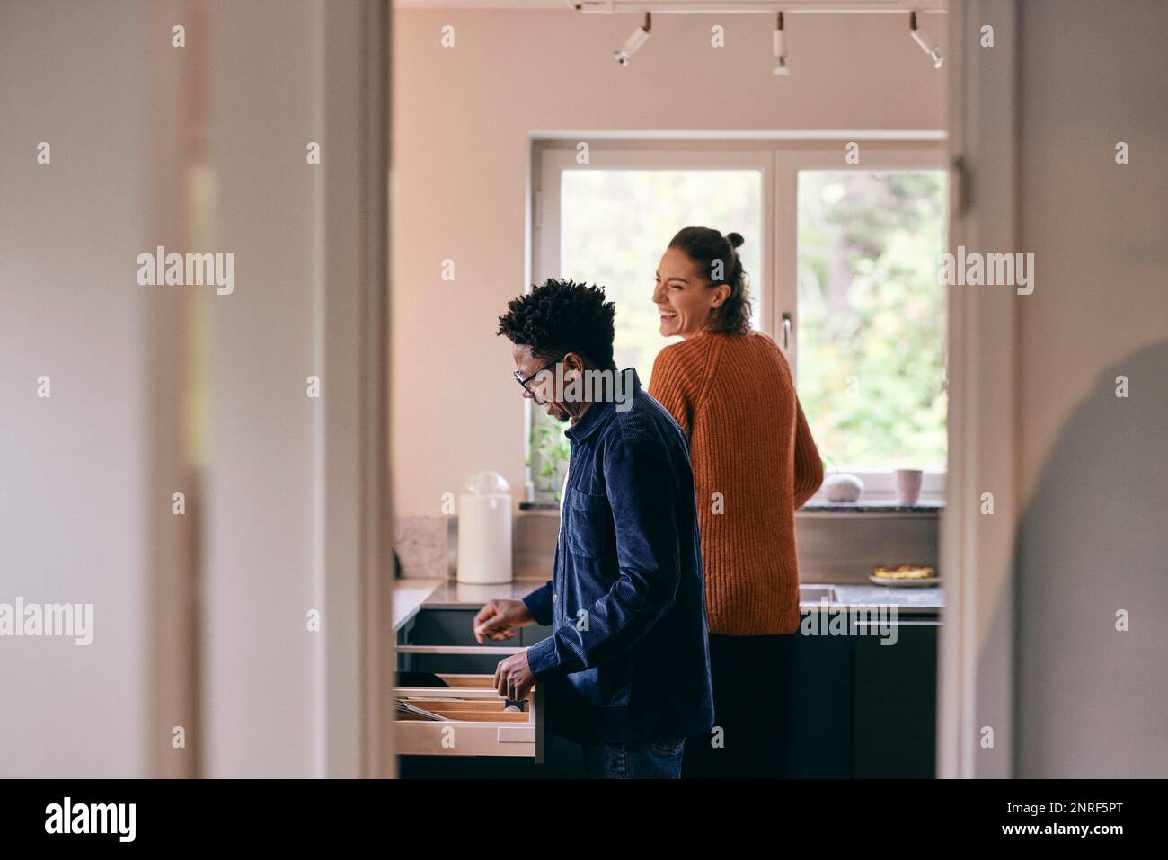 Happy multiracial couple helping each other while standing in kitchen at home Stock Photo