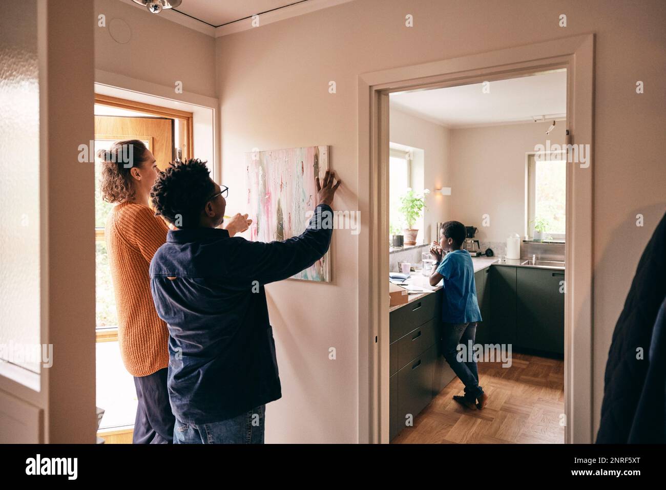 Father and mother hanging painting on wall with son standing in kitchen at home Stock Photo