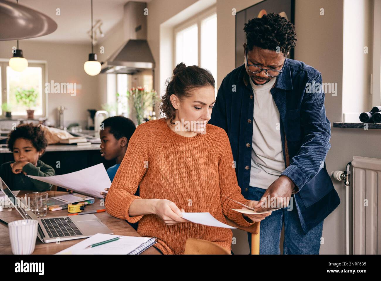 Multiracial couple discussing over financial bills while sons in background at home Stock Photo
