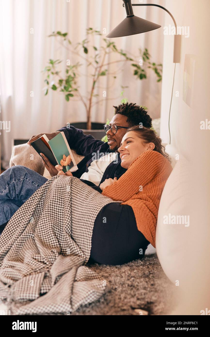 Man and woman reading books while sitting on sofa at home Stock Photo