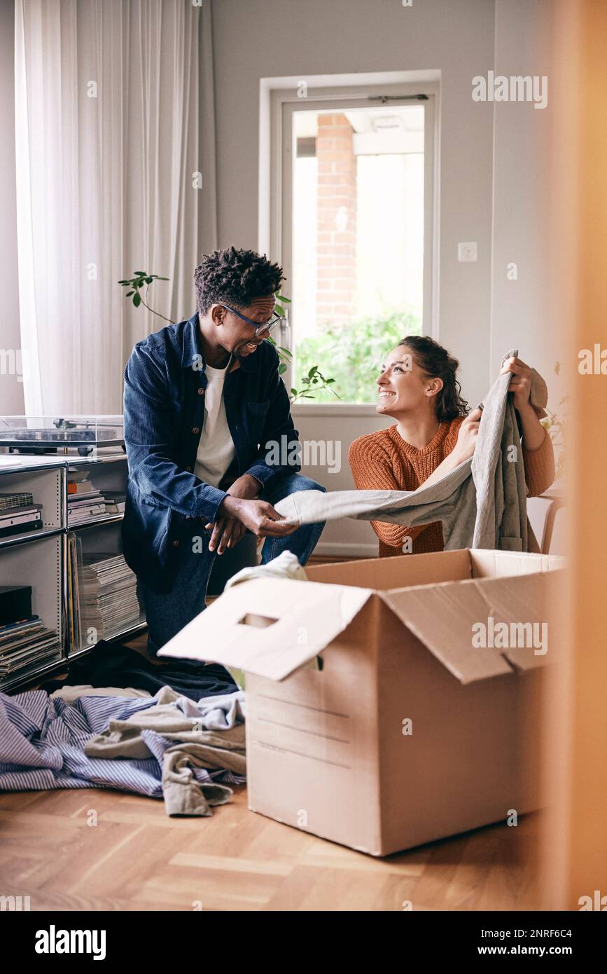 Couple talking to each other sorting out clothes from cardboard box at home Stock Photo