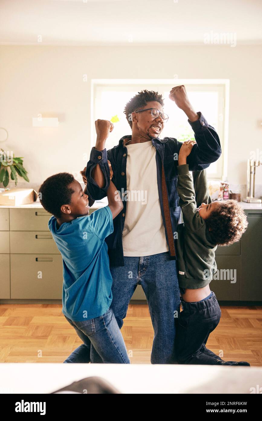 Playful father lifting sons in arms while standing at home Stock Photo