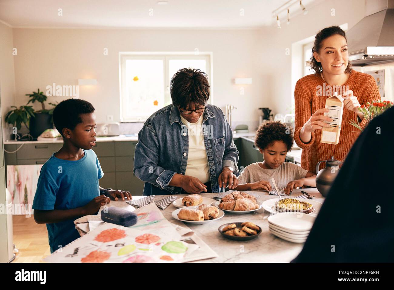 Family helping each other while preparing breakfast on kitchen island at home Stock Photo