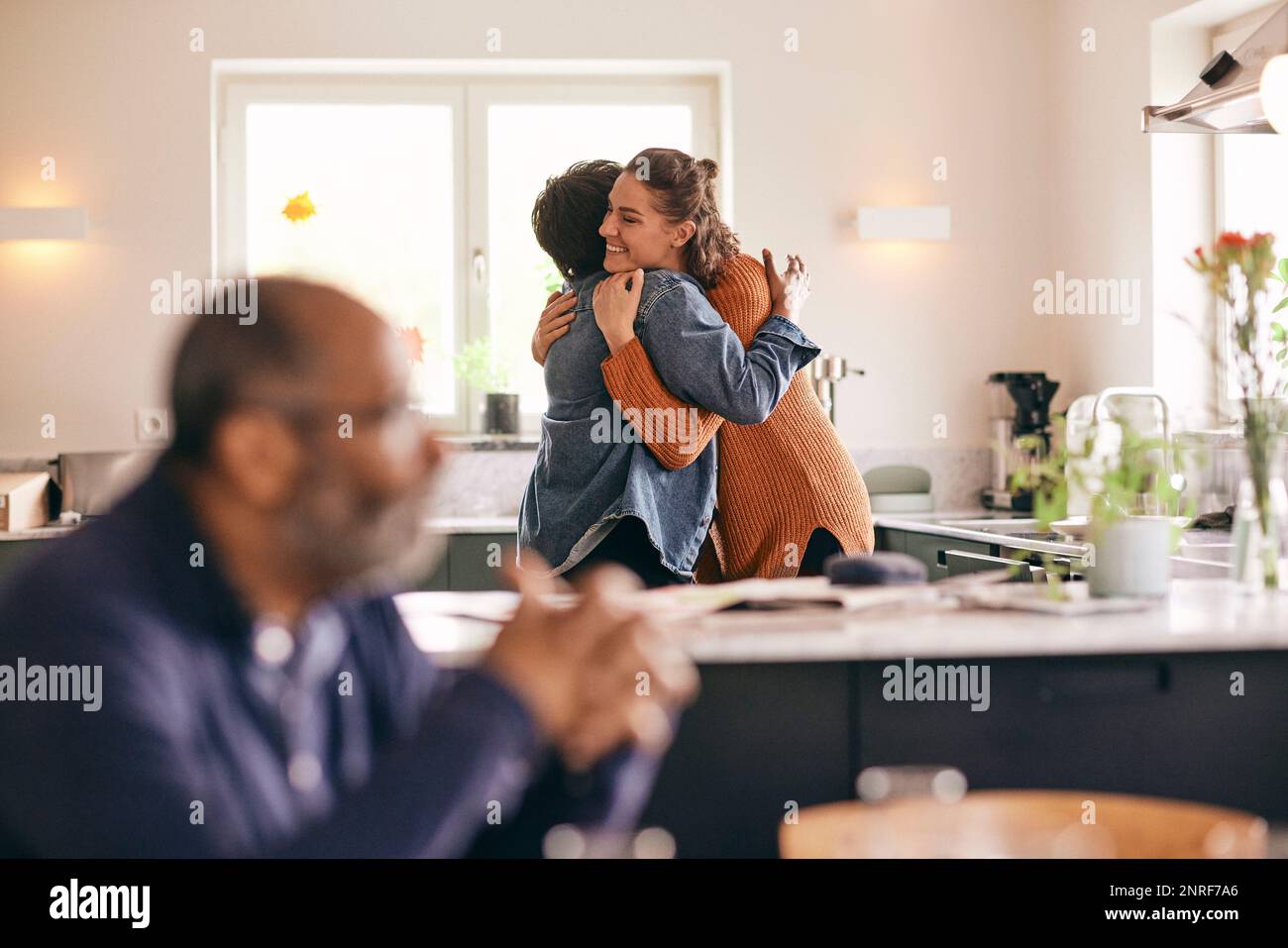 Smiling woman embracing mother-in-law while standing in kitchen at home Stock Photo
