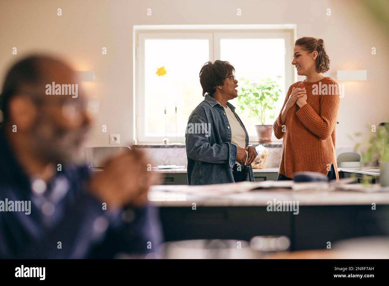 Woman with hands on chest talking to mother-in-law standing in kitchen at home Stock Photo