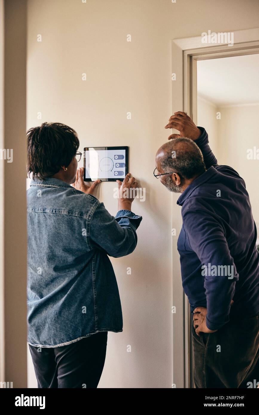Senior couple looking at home automation on wall Stock Photo