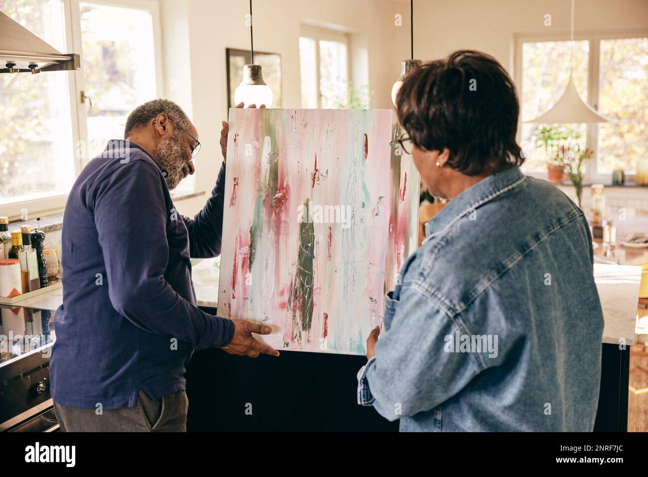 Senior couple helping each other while holding painting at home Stock Photo