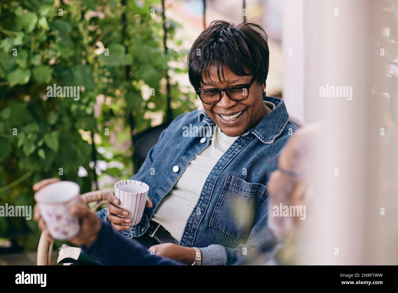 Happy senior woman wearing denim jacket enjoying drink with man Stock Photo