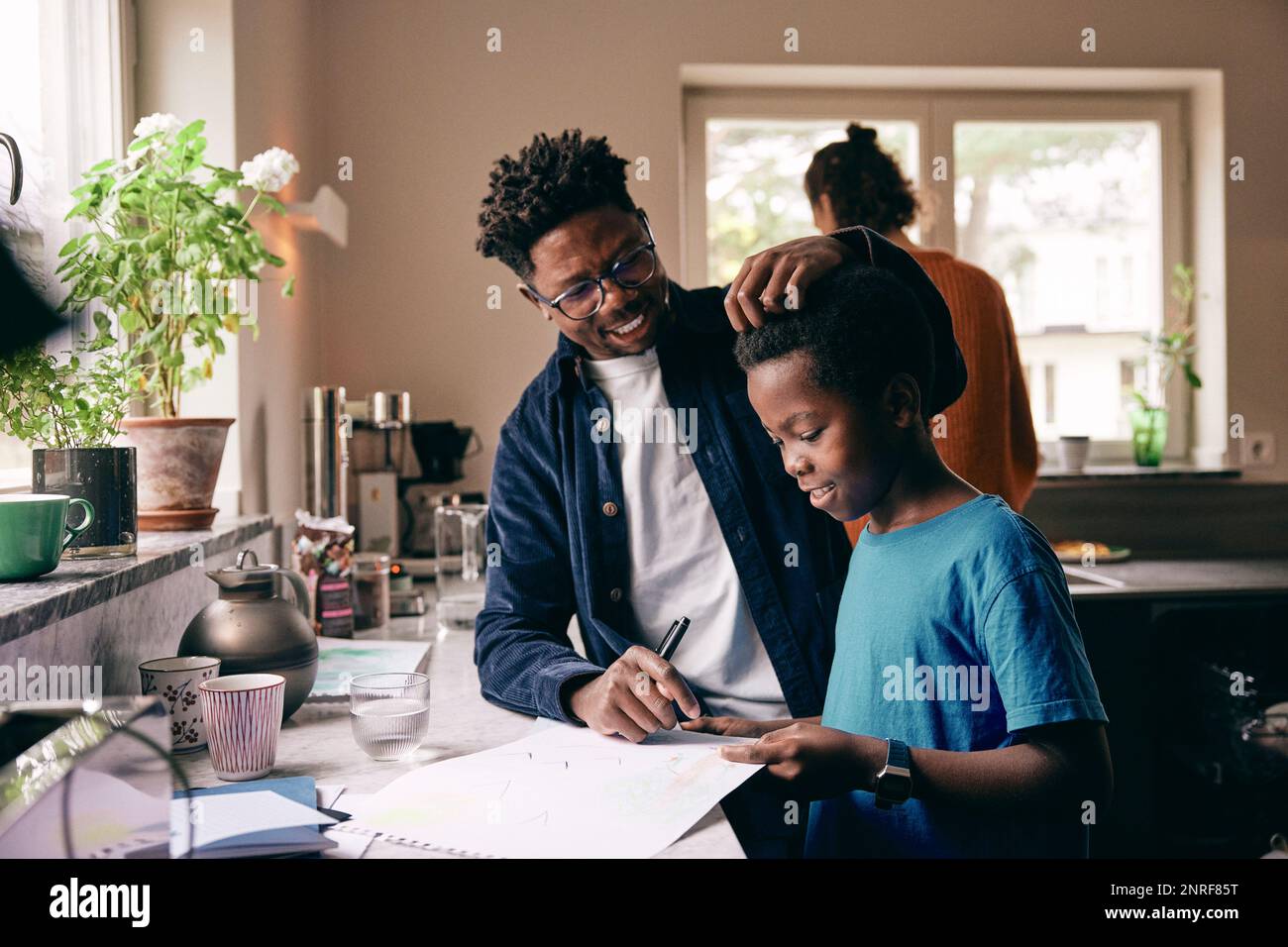 Smiling father caressing hair of son doing homework at home Stock Photo
