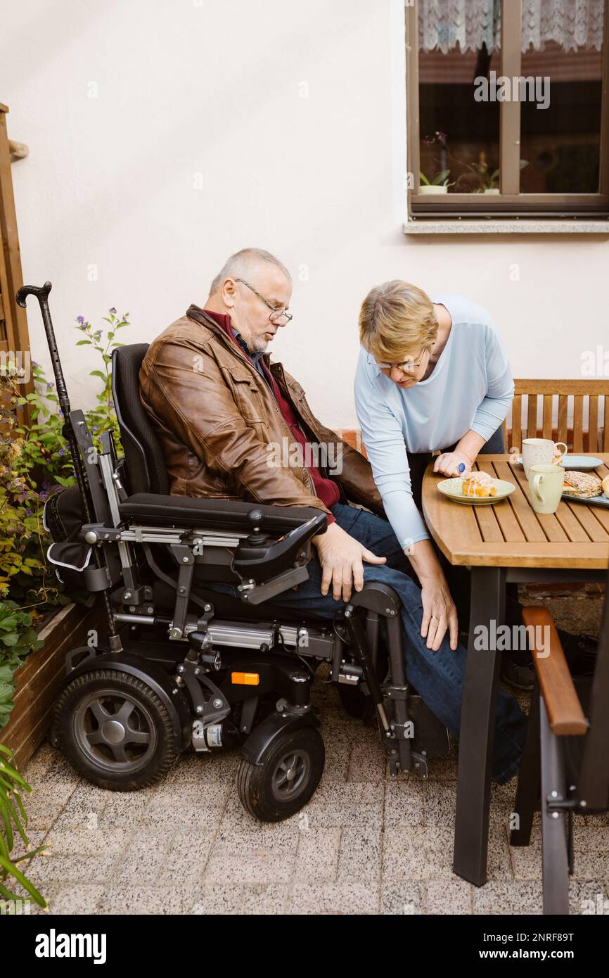 Senior woman assisting man in motorized wheelchair with disability at backyard Stock Photo