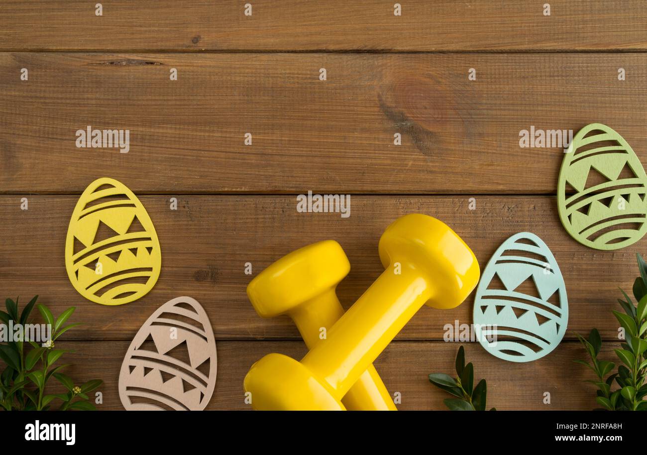 Dumbbells, boxwood branches, Easter wooden decorations. Healthy fitness composition, gym workout and training concept. Flat lay with copy space. Stock Photo
