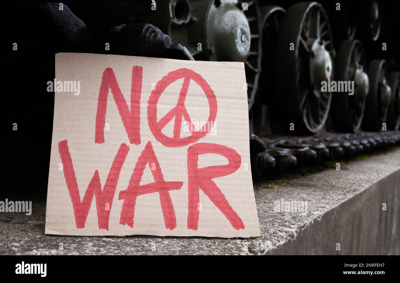 No War placard with peace sign on army tank caterpillar continuous track wheels. Military armored tracked fighting vehicle with anti-war banner. Stock Photo