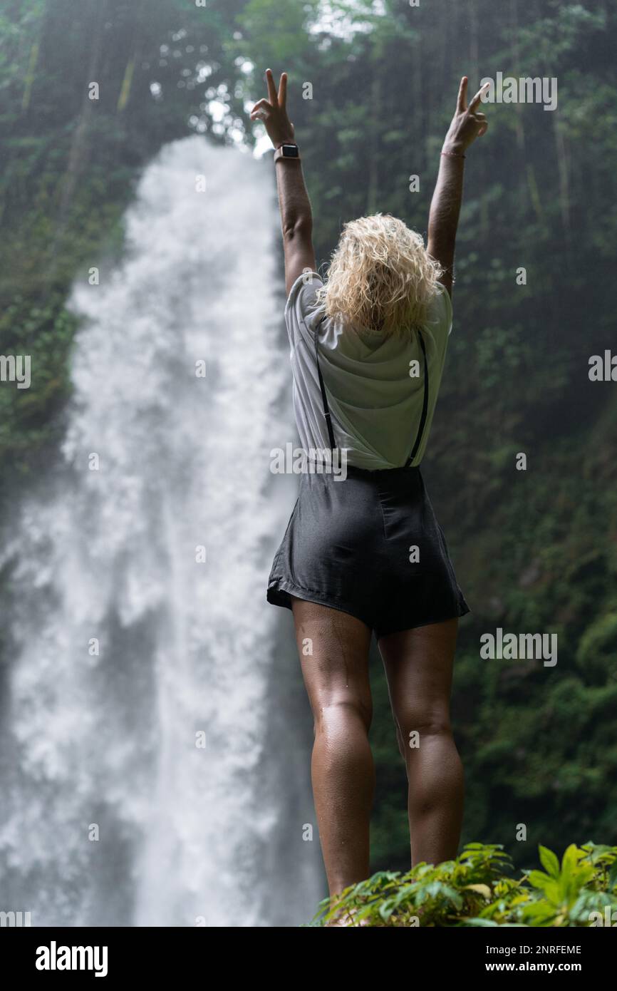A woman stands on a rock and looks at a waterfall in the jungle Stock ...