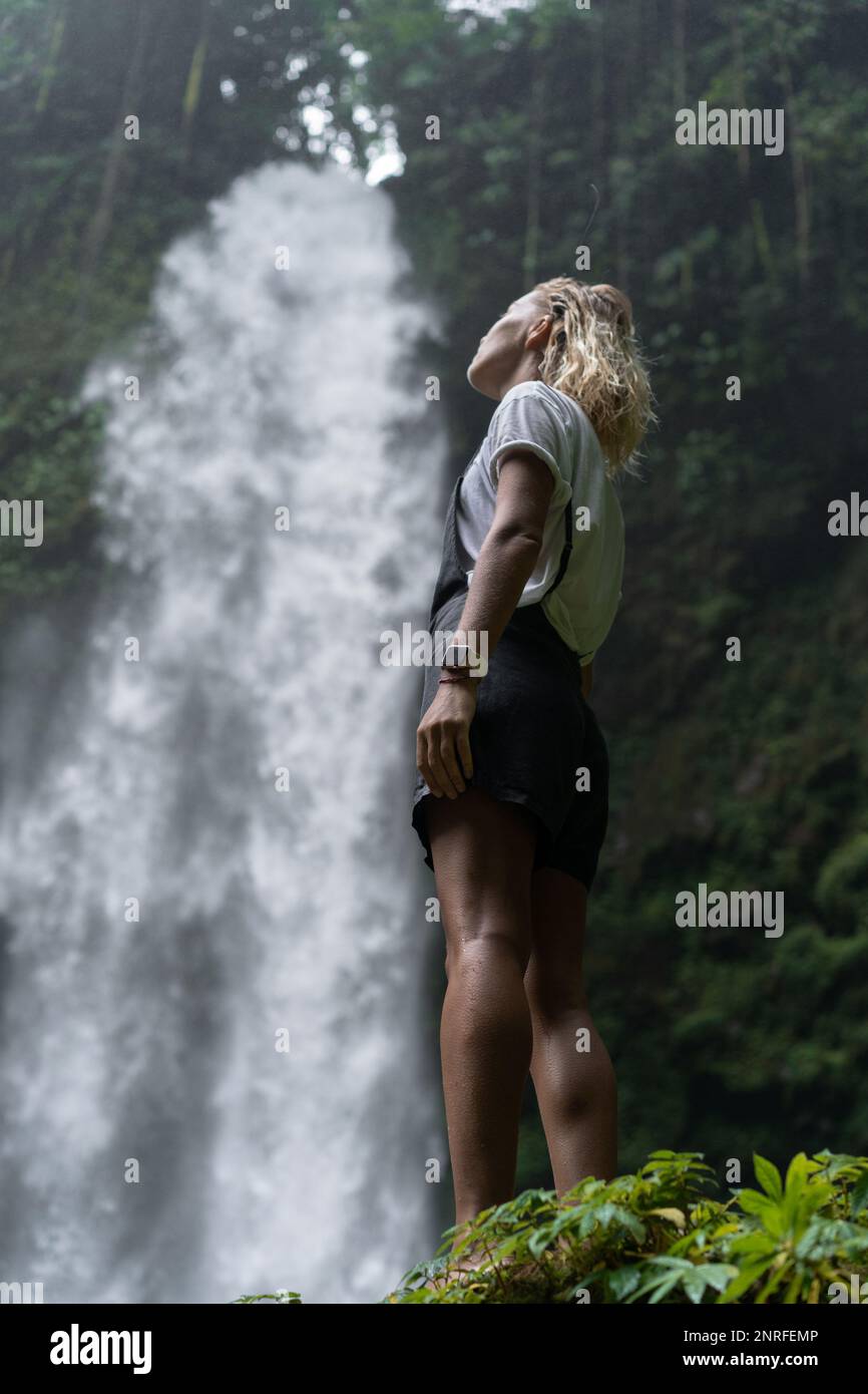 A woman stands on a rock and looks at a waterfall in the jungle Stock ...