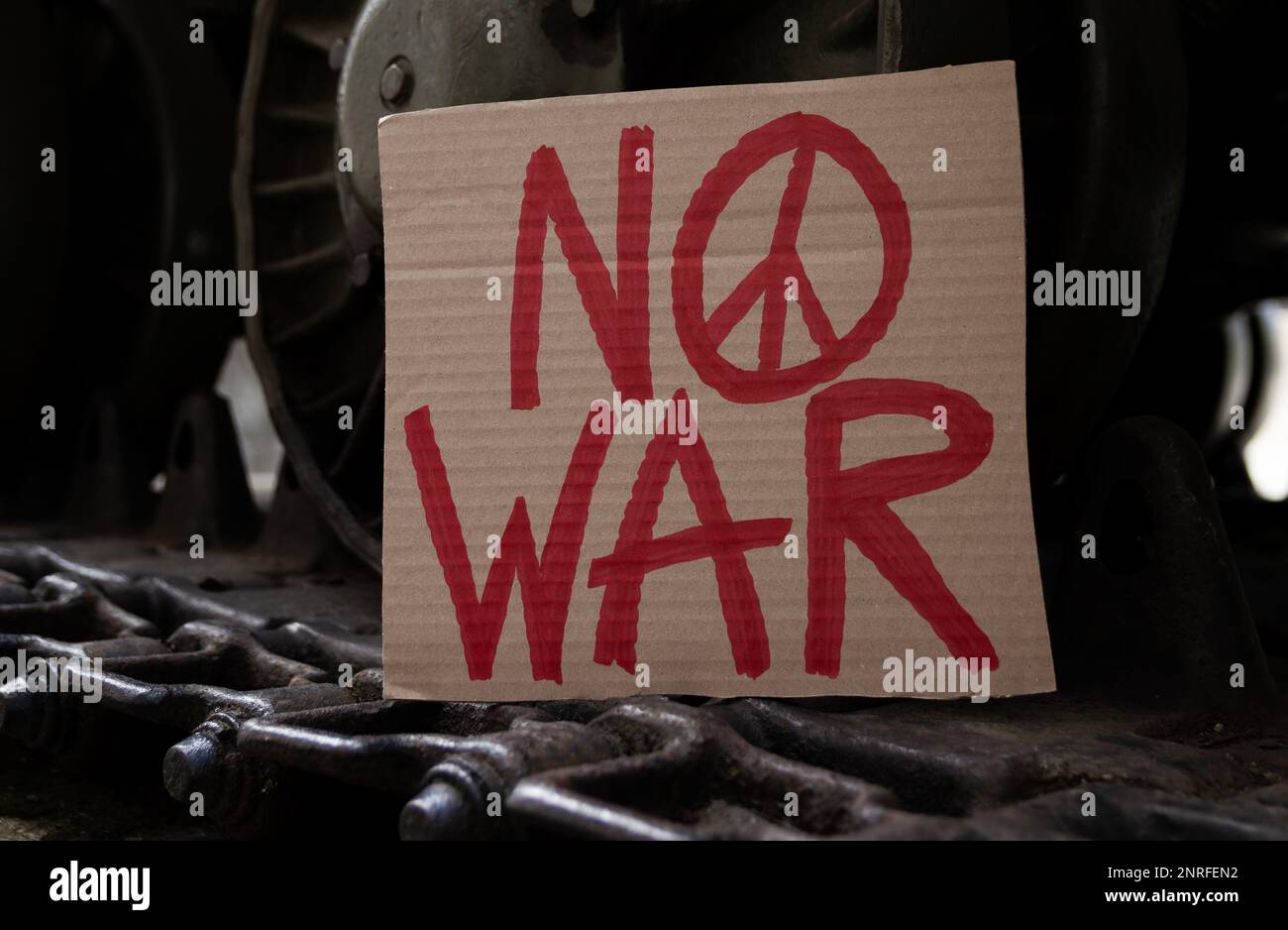 No War placard with peace sign on army tank caterpillar continuous track wheels. Military armored tracked fighting vehicle with anti-war banner. Stock Photo