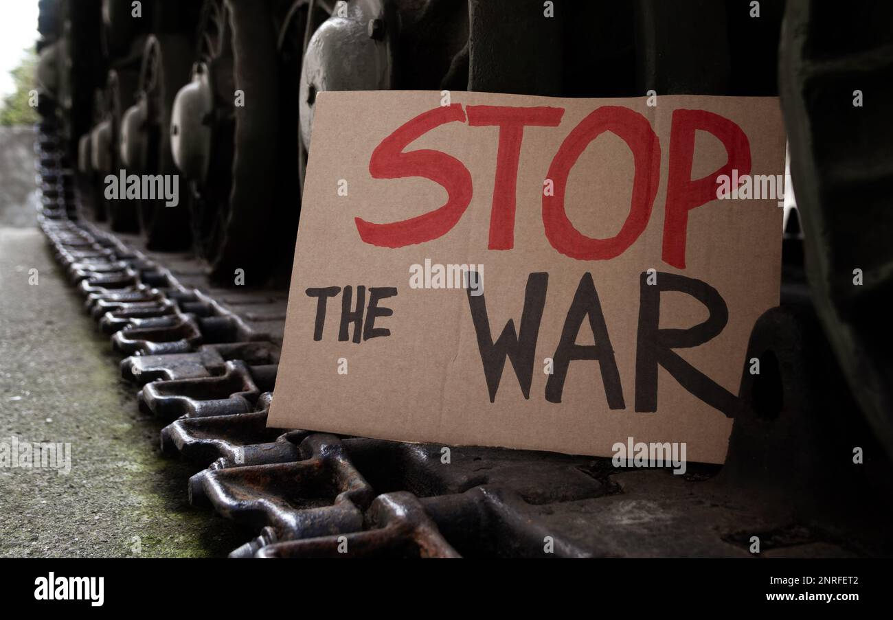 Stop the War placard sign on army tank caterpillar continuous track wheels. Military armored tracked fighting vehicle with anti-war banner. Stock Photo