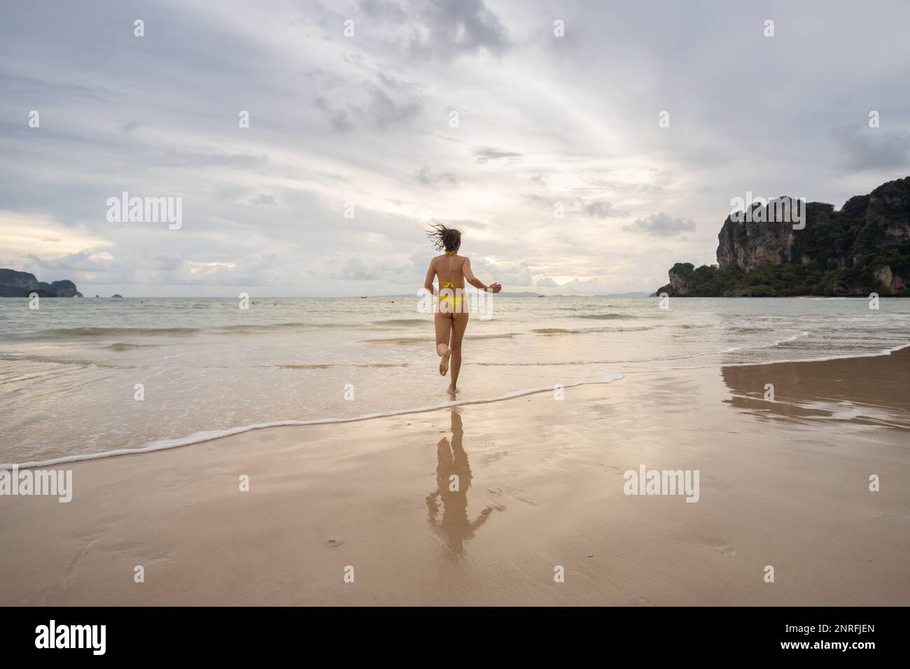 Woman wearing yellow bikini running on Railay Beach at sunset Stock