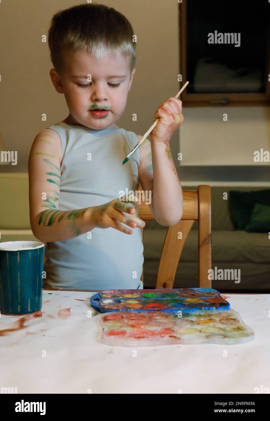 The boy is engaged in creativity he paints his hands with paint Stock